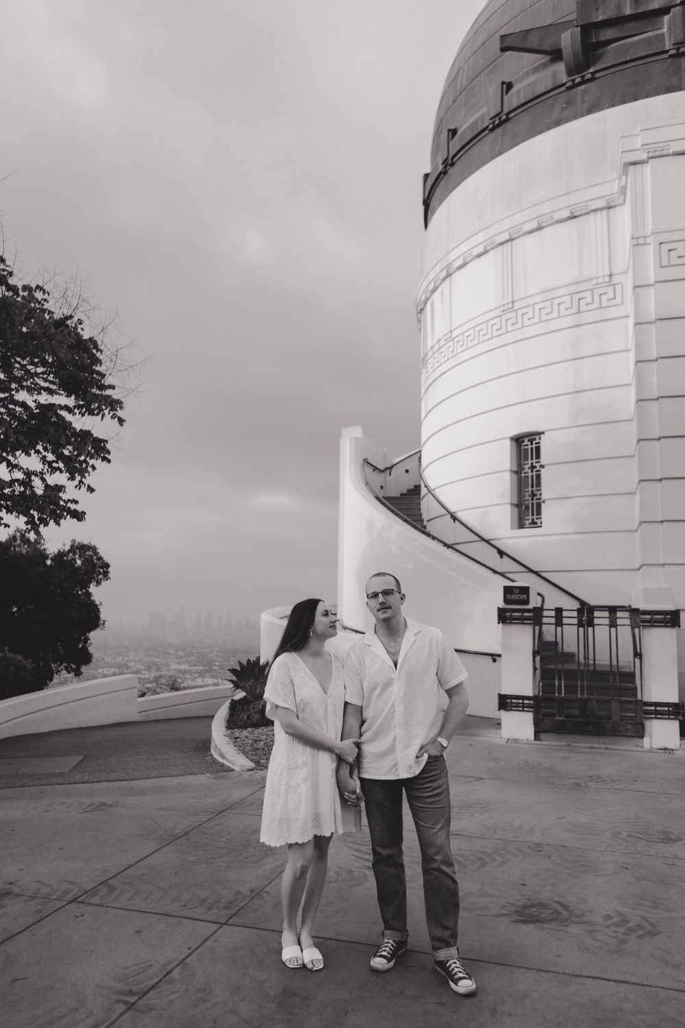 A couple poses together outside the iconic Griffith Observatory in Los Angeles on an overcast day.
