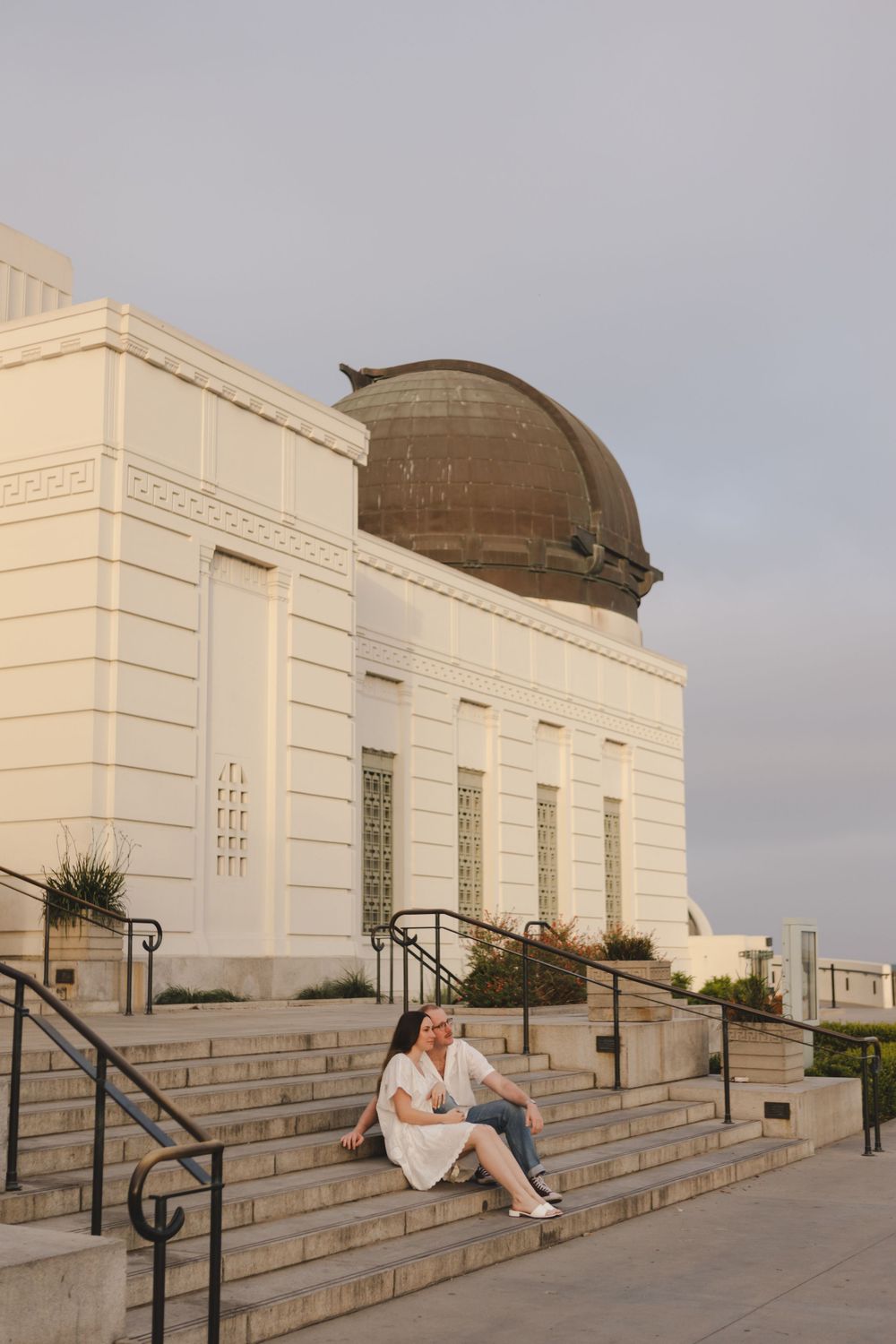 A couple sits on the steps of the Griffith Observatory at dusk.