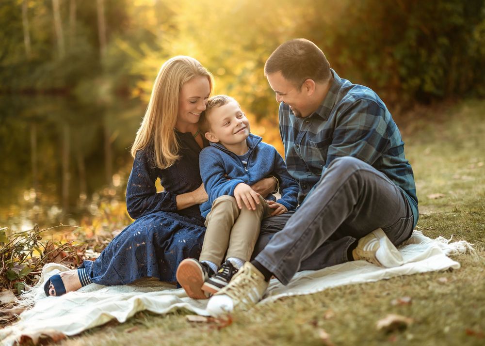 Family sharing joyful moment together while sitting on blanket in golden autumn sunlight.