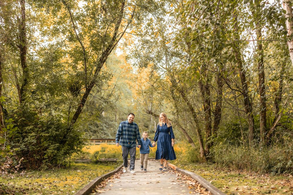 A group of people walk along a tree-lined autumn path with golden leaves falling in the late afternoon sunlight.