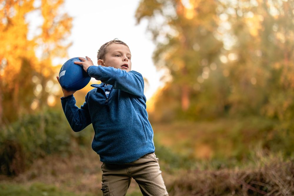 A person wearing a blue sweater and brown pants walks through an autumn forest at sunset.
