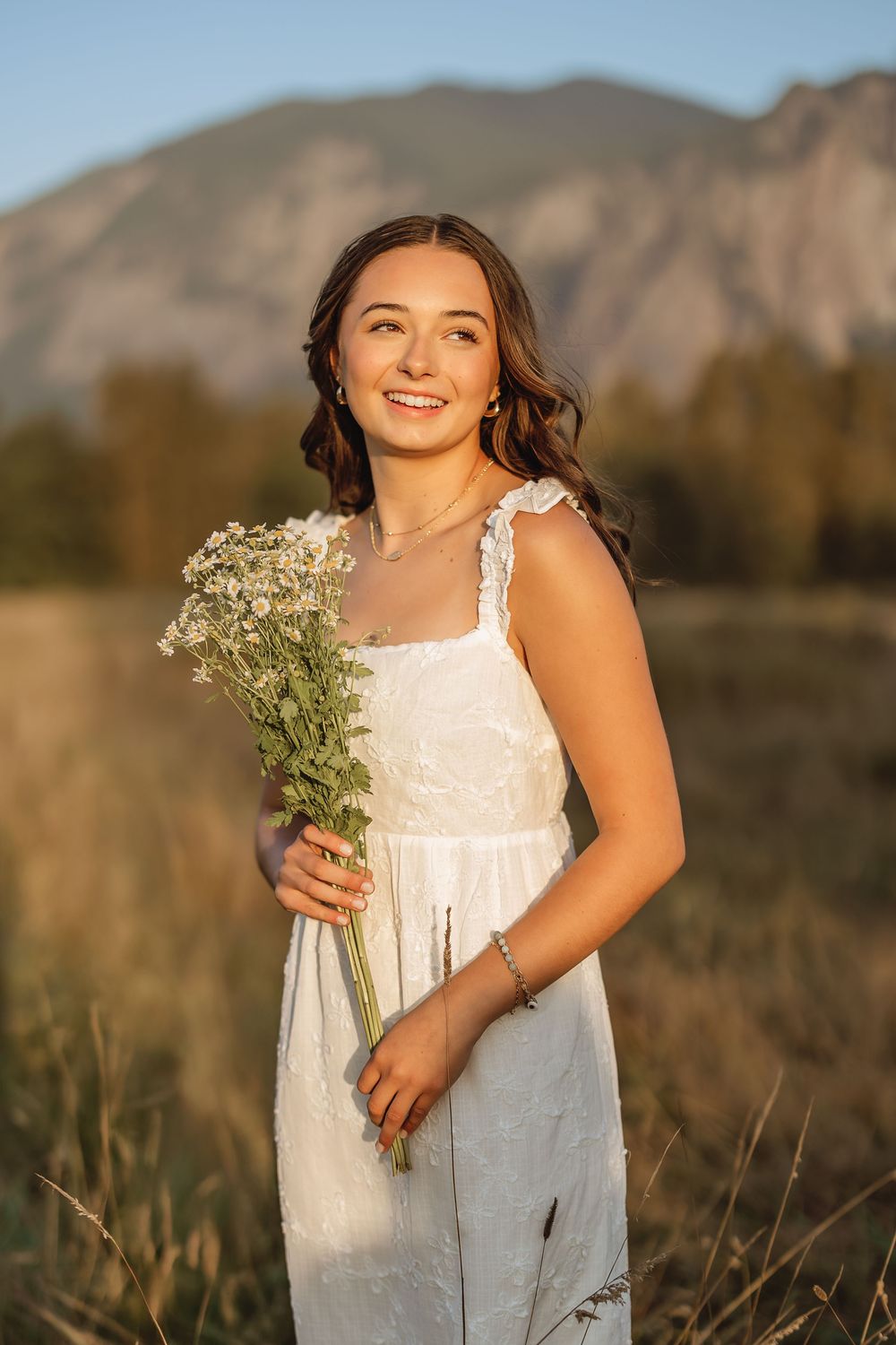 Summer portrait session with white dress and baby's breath flowers against mountain backdrop.