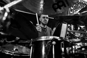A close-up shot of a drummer performing on stage with a drum kit and cymbals in a dark concert setting.