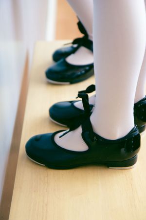 Close-up view of black tap shoes on wooden floor with white tights showing classic dance attire.
