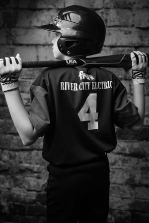 A black and white photo showing a baseball player holding a bat against a brick wall background.