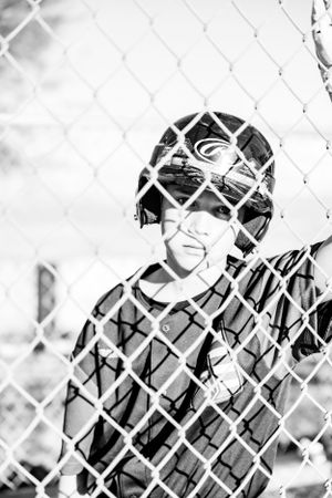 Baseball player watch from behind a chain link fence in a black and white dugout scene.