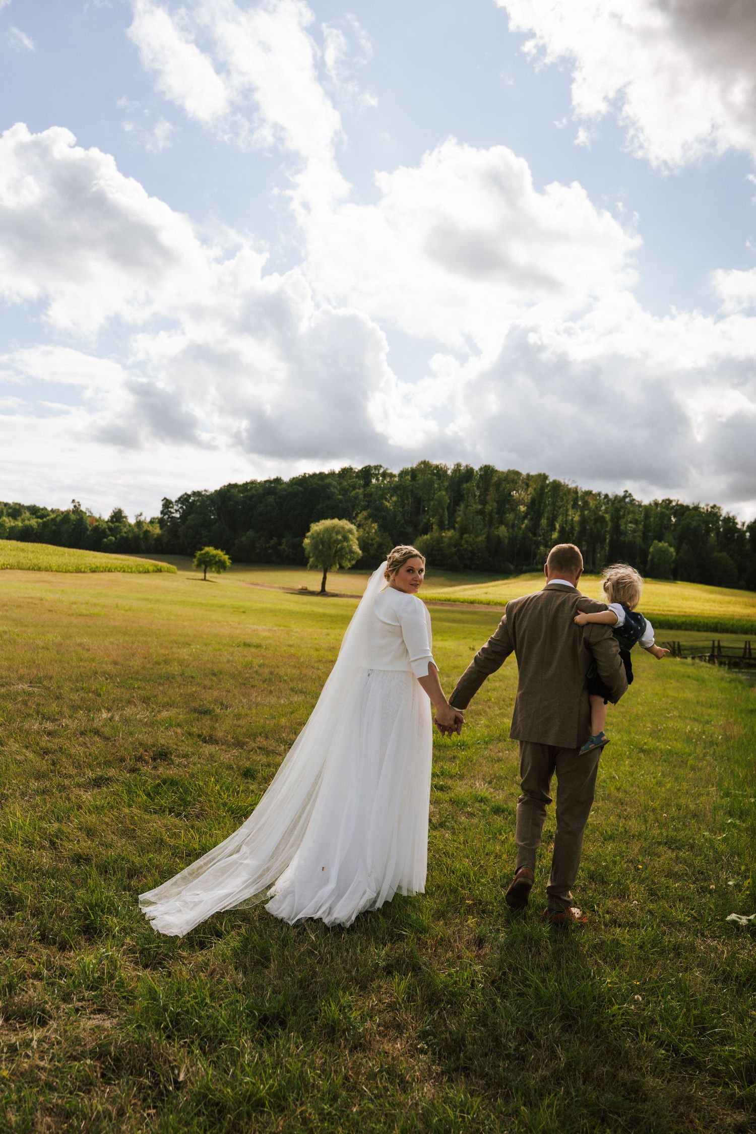 A dramatic wedding photo in a sunlit forest clearing with tall trees creating natural framing.
