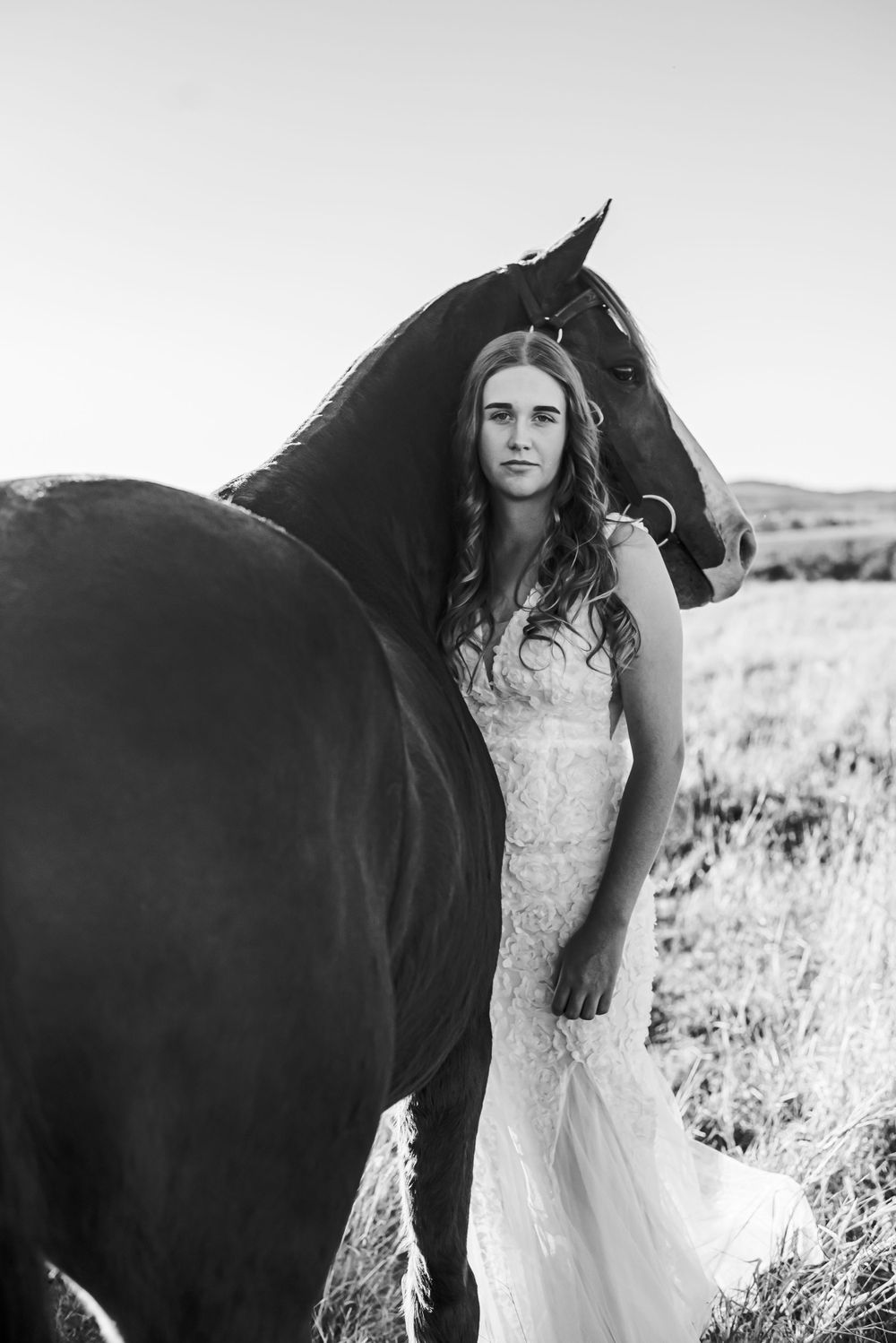 Black and white image of a horse and white dress against a serene field backdrop.