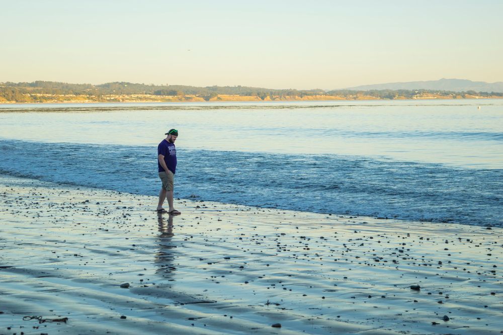 Person walking along the shoreline during sunset at a peaceful beach.