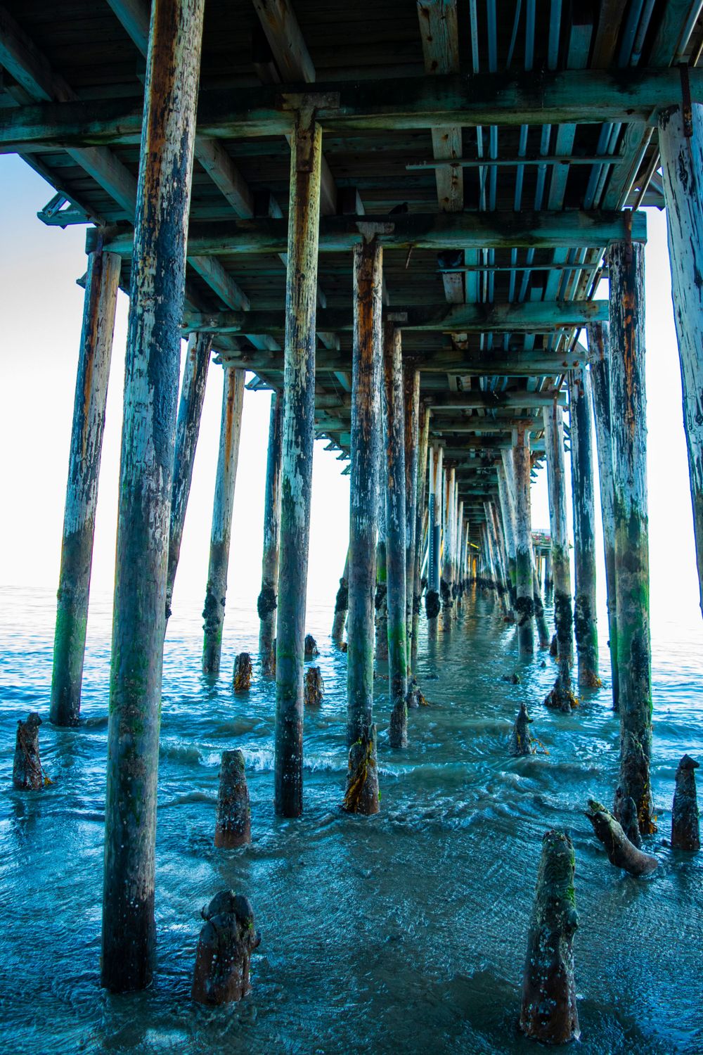Underneath view of wooden pier posts creating dramatic perspective over ocean waves.