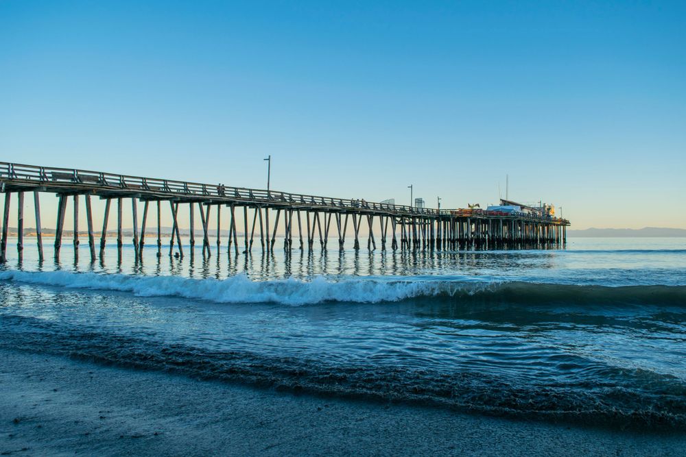 Long wooden pier extends into calm ocean waters under clear morning sky.
