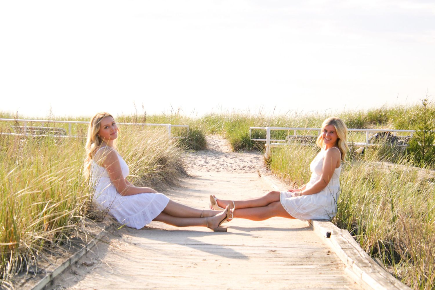 Peaceful beachside photo session with white dress against coastal dunes and fencing.
