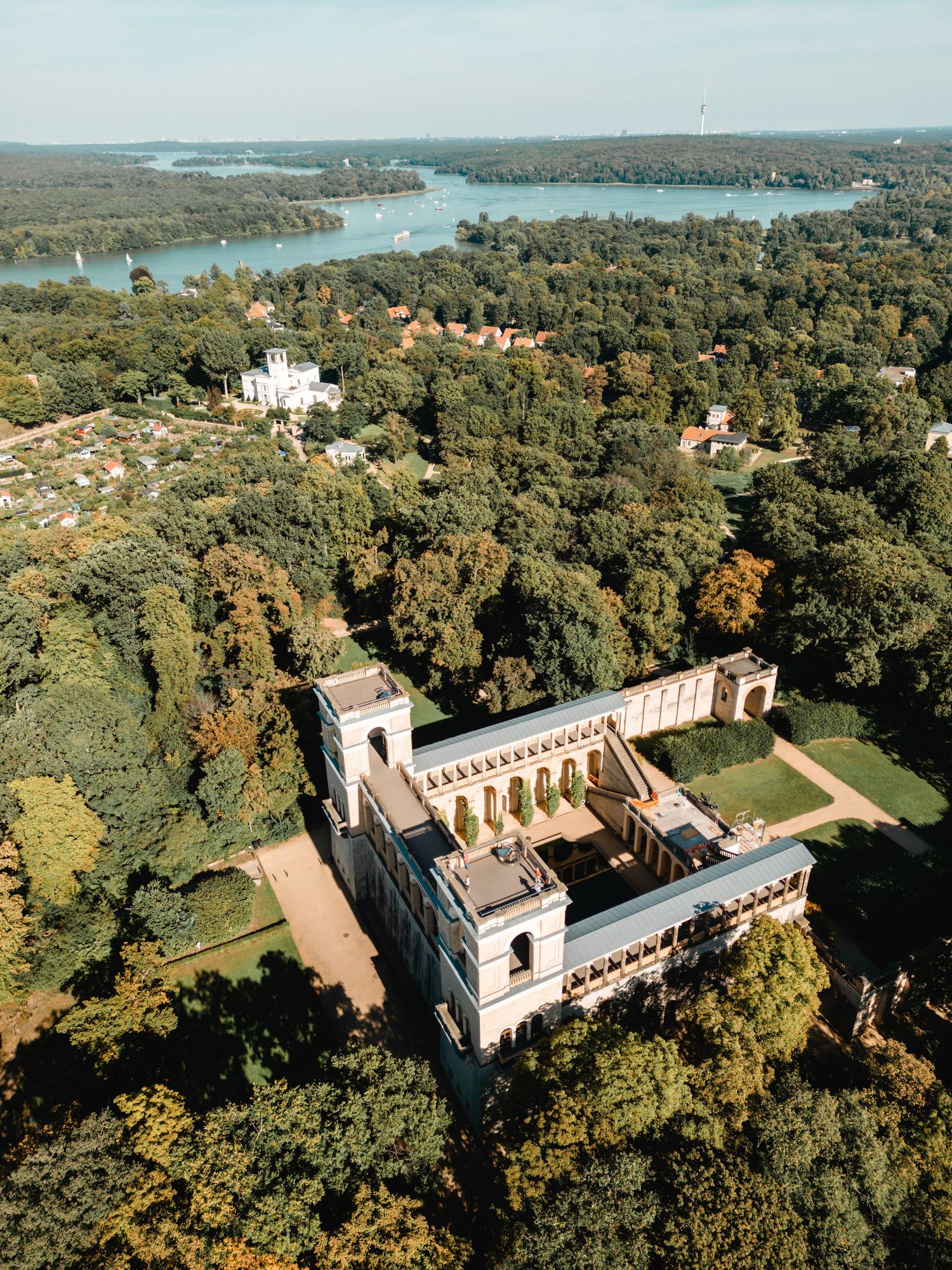 Aerial panoramic view of an ornate historic stone castle surrounded by dense forest and waterways in autumn colors.
