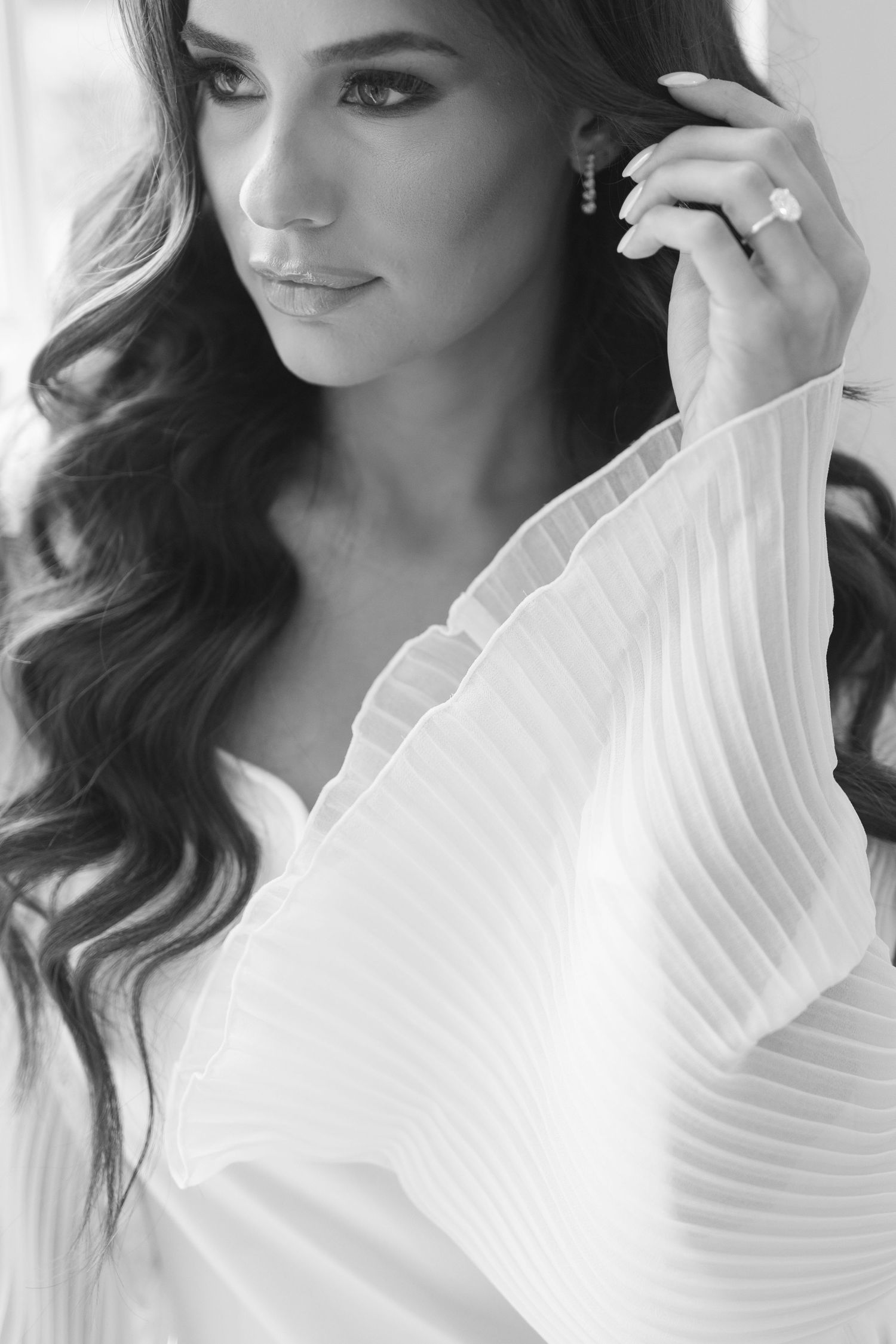 Black and white portrait of a beautiful bride with wavy hair wearing a white pleated robe and diamond engagement ring.