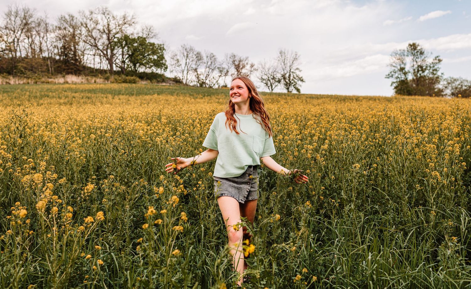 A joyful young woman runs through a vibrant yellow wildflower field on a sunny day.
