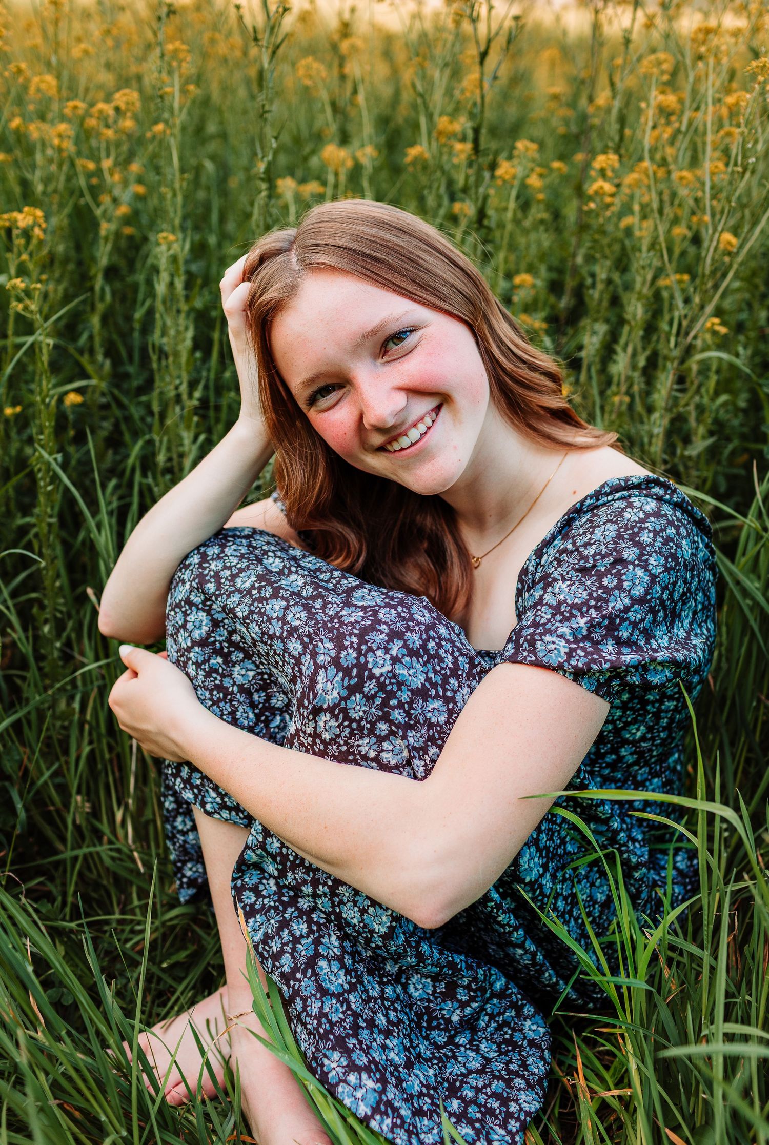 Young woman in floral dress smiling in a field of wildflowers during golden hour photography session.