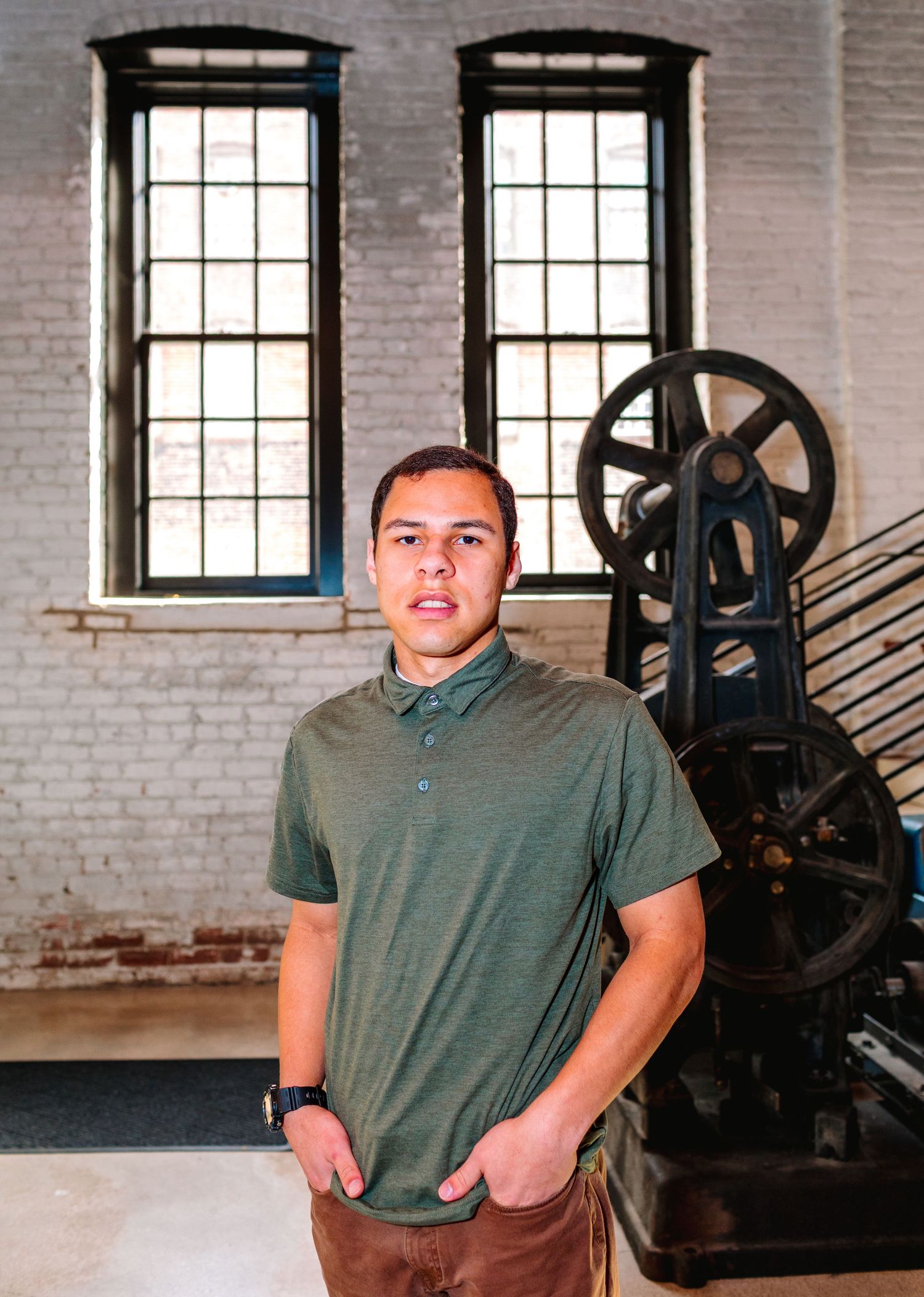 Young man in green polo shirt posing in industrial brick building interior.