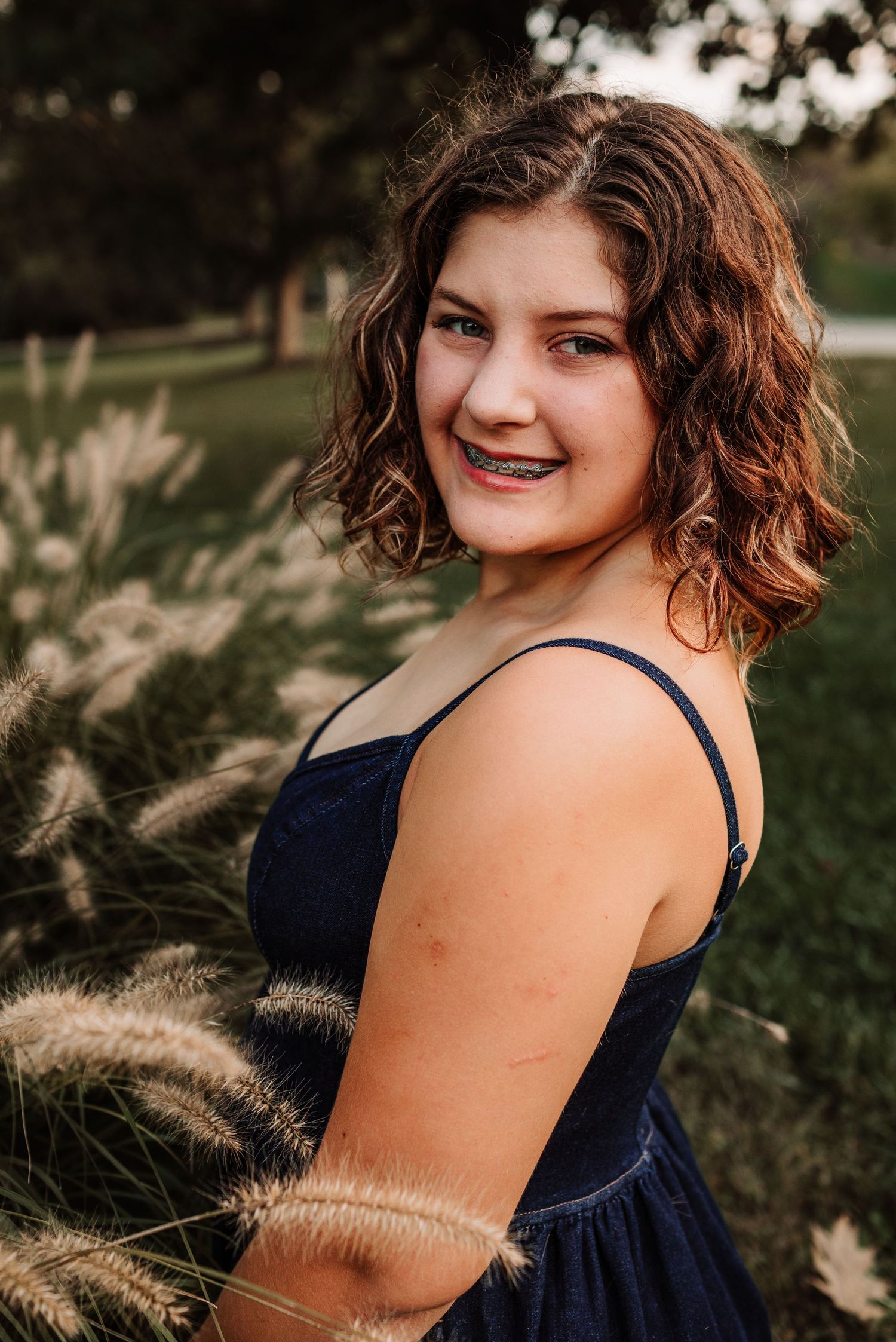 Teenage girl with braces in navy dress smiling among ornamental grasses.