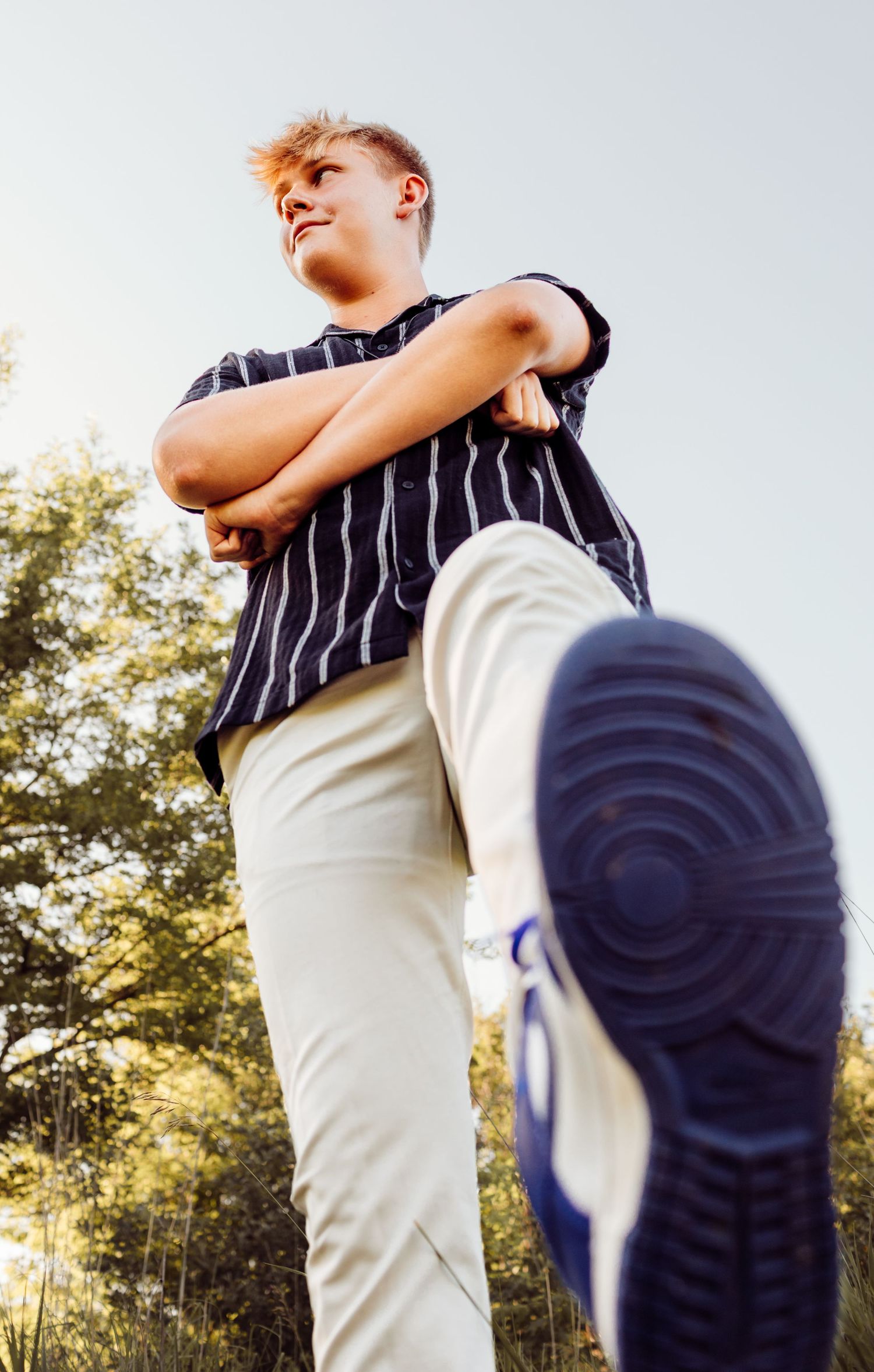 Low angle view of teenage boy in striped shirt and blue sneakers posing outdoors.