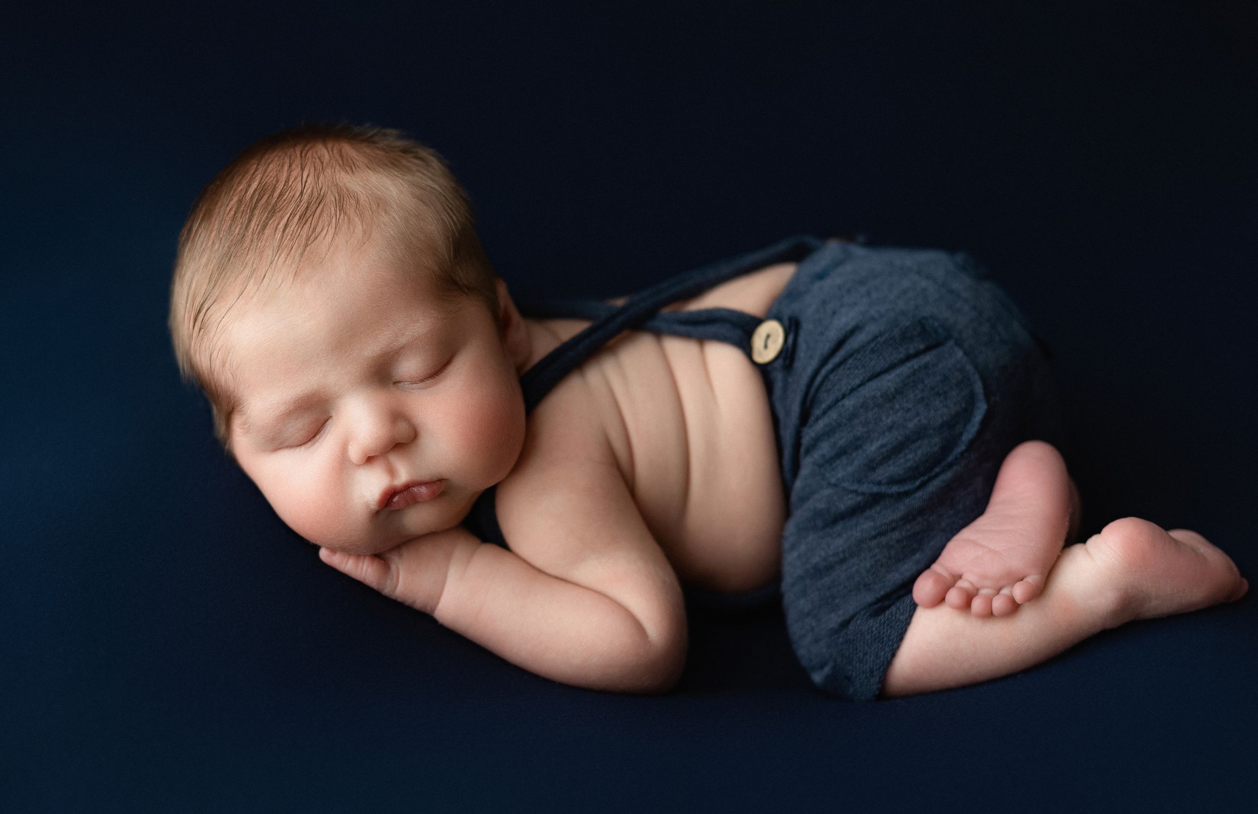 a newborn boy with chunky cheeks wearing overalls. Greenville SC newborn photographer. - Easley Sc newborn photographer. Greenville SC photo