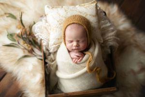 A newborn girl with a mustard-colored hat and mustard-accent flowers. Greenville SC newborn photographer. - Easley Sc newborn photographer.