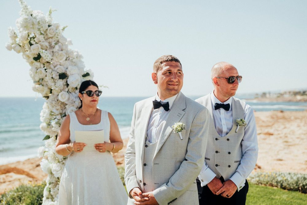Beautiful outdoor beach wedding ceremony with floral arch and ocean backdrop on sunny day.