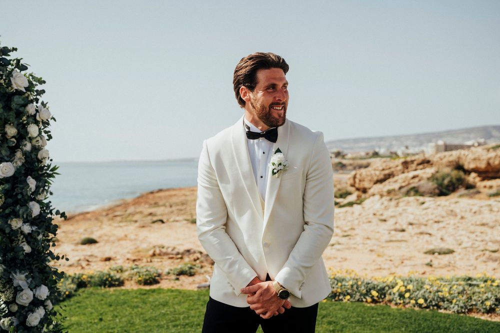 Person in a white suit jacket stands in a desert landscape with mountains in the background.