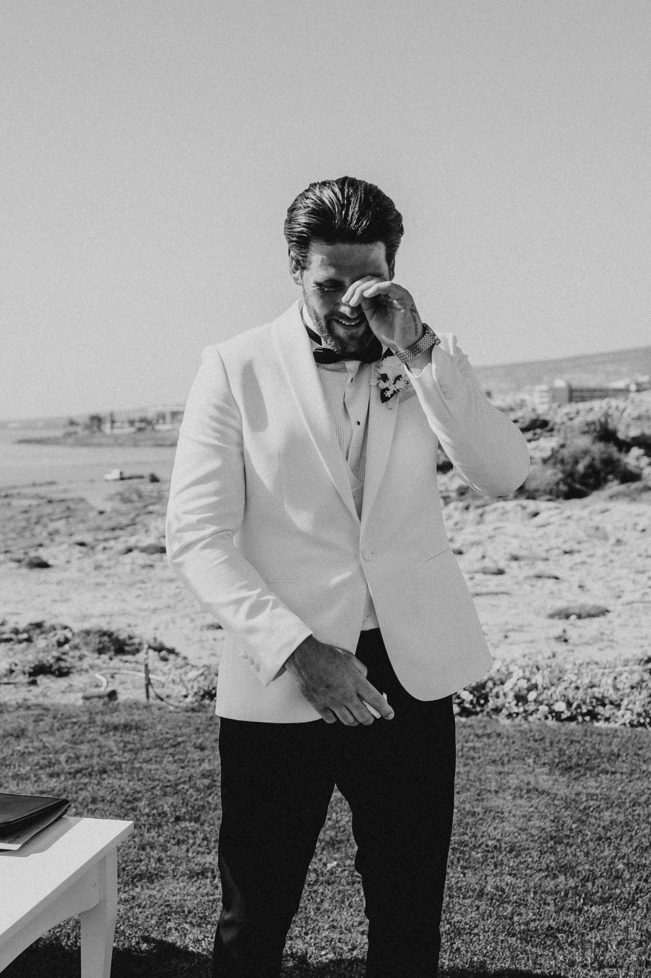 Black and white photos show emotional moments of someone in a white suit jacket during what appears to be a wedding.