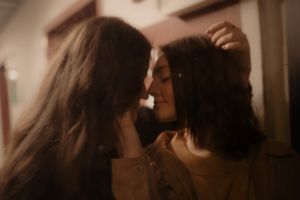 Two women sharing an intimate moment, leaning close together in a warmly lit room.