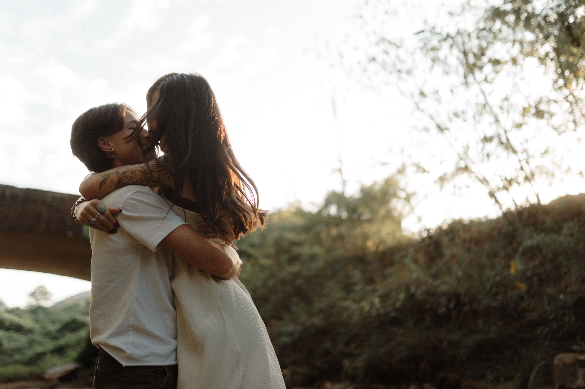 A tender embrace captured during golden hour with sunlight streaming through trees.