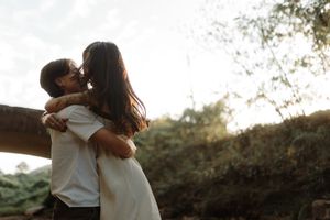 A tender embrace captured during golden hour with sunlight streaming through trees.