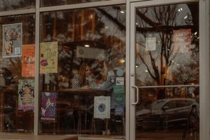 Cozy cafe storefront with colorful flyers on glass windows reflecting bare trees at dusk.