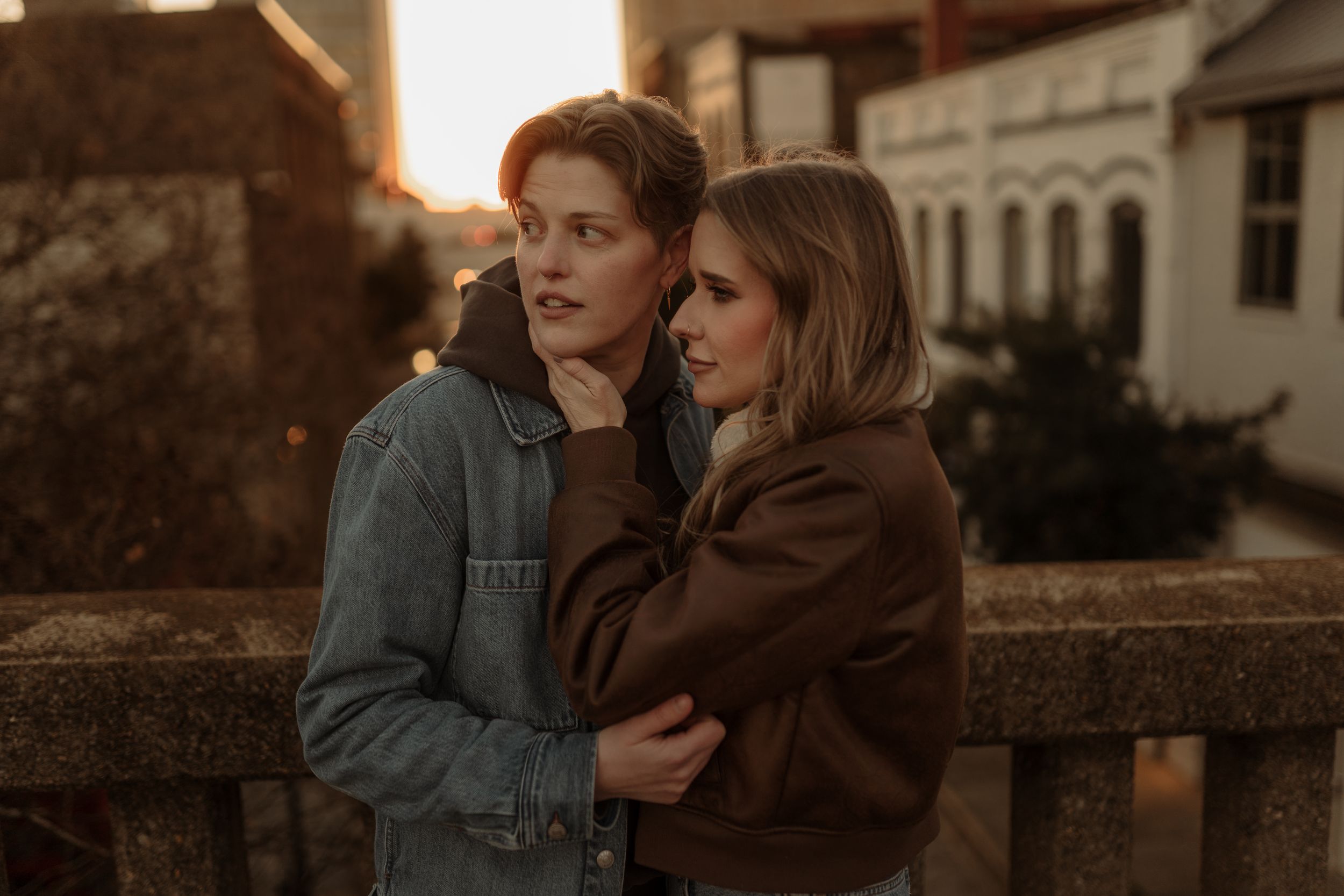 Couple embracing during sunset against historic stone building backdrop.