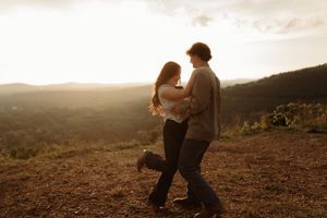 Couple dancing romantically at golden hour sunset on a hilltop with scenic mountain valley views in the background.