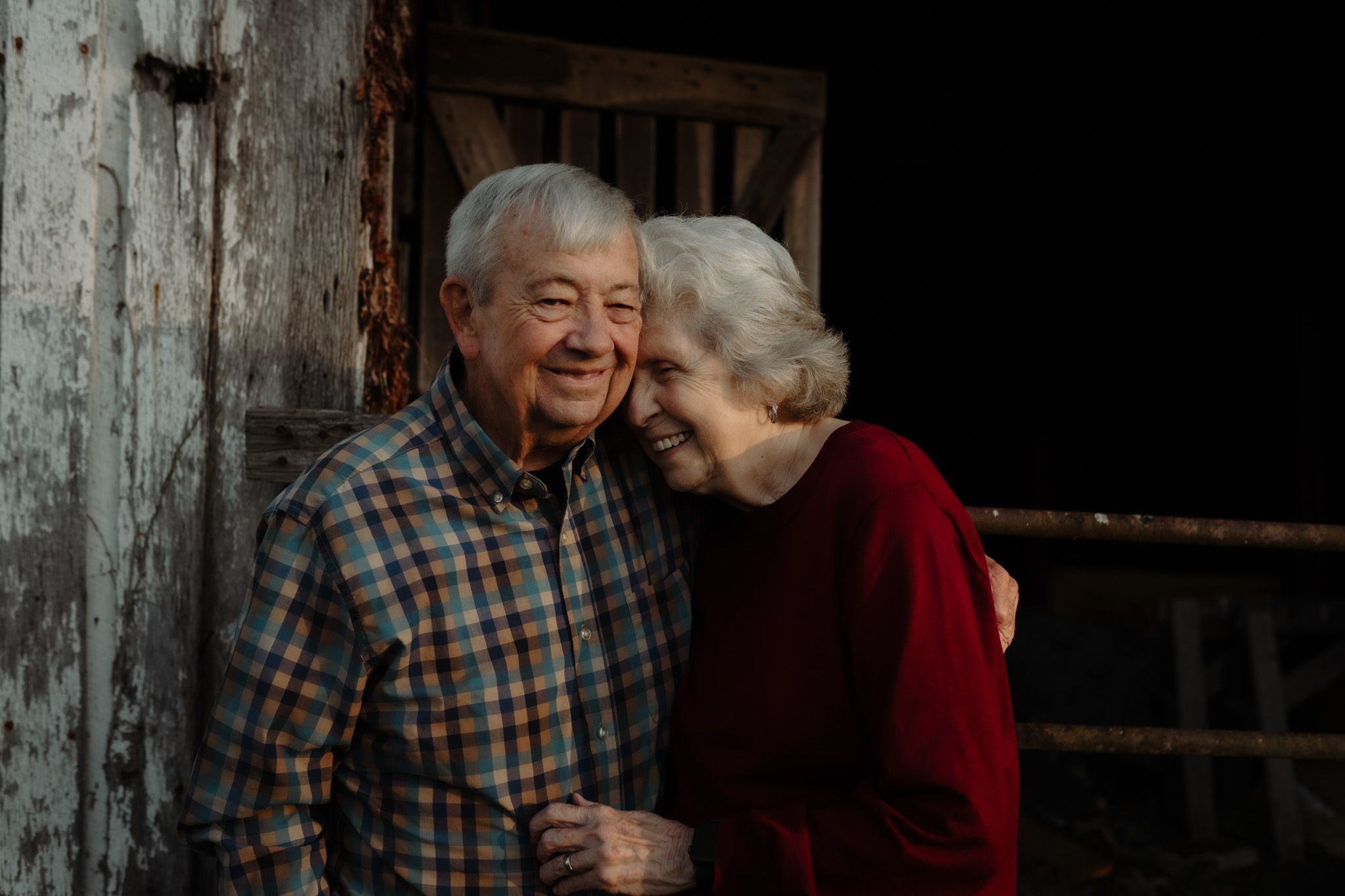 An elderly couple shares a tender moment outside a rustic wooden building.
