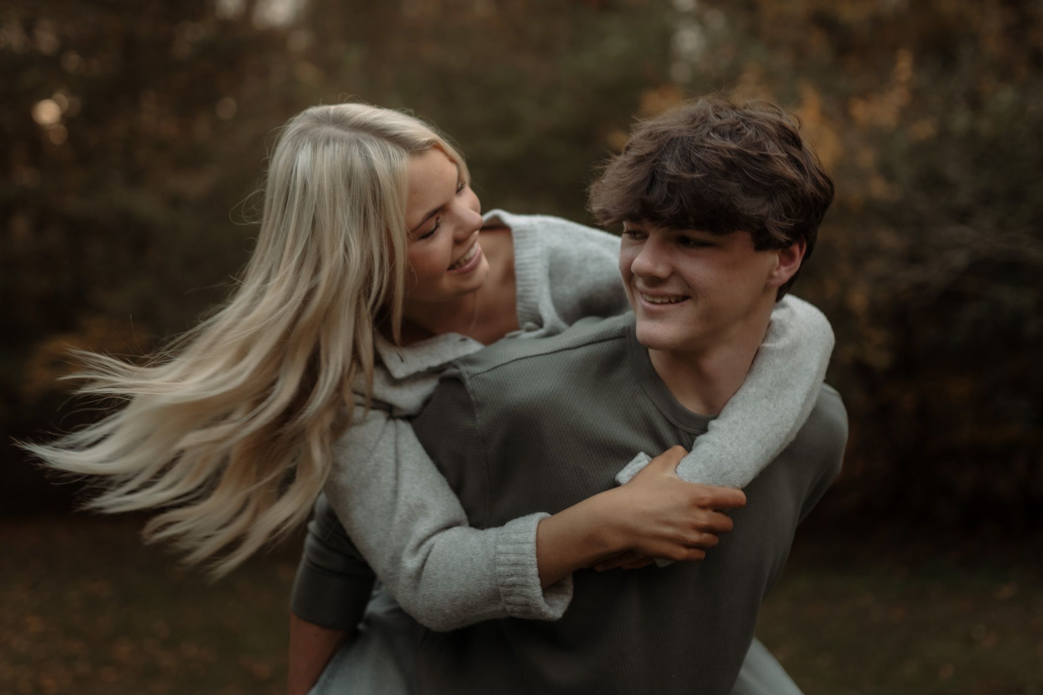 A romantic couple embraces and laughs together during a sunset photoshoot in a natural outdoor setting.