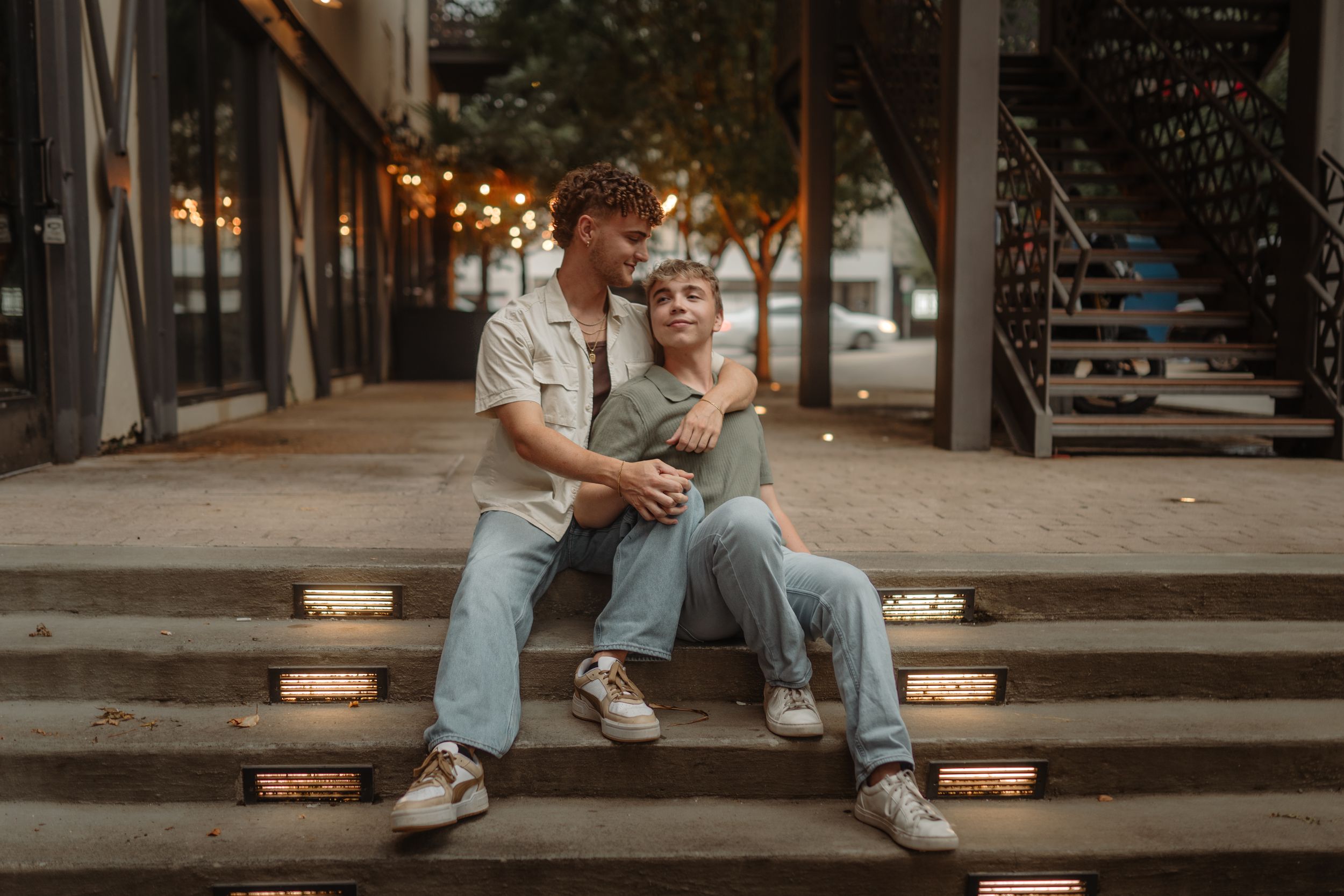 Couple sitting casually on urban concrete steps in casual attire during a photoshoot.