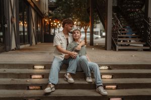 Couple sitting casually on urban concrete steps in casual attire during a photoshoot.
