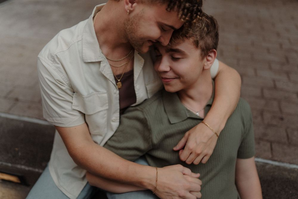 Romantic couple in casual attire sharing intimate moments while sitting together outdoors on brick pavement.