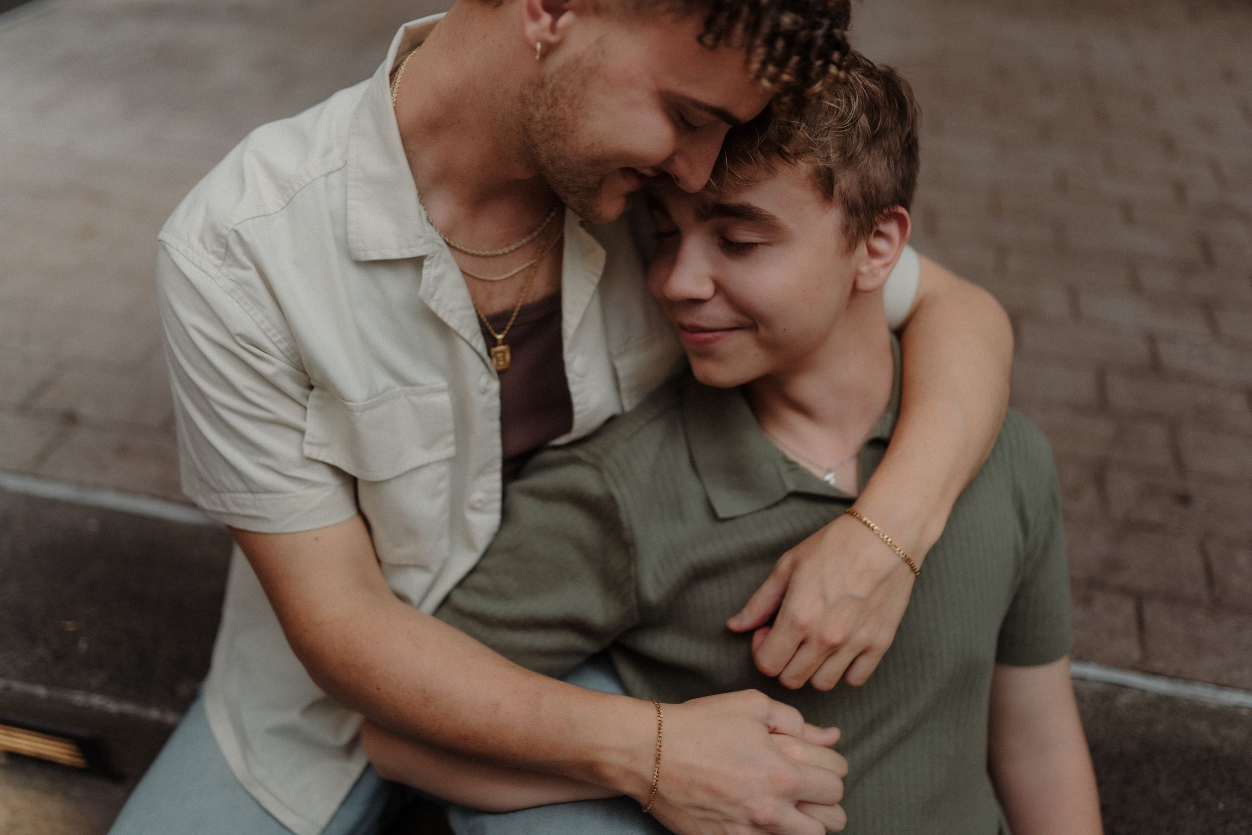Romantic couple in casual attire sharing intimate moments while sitting together outdoors on brick pavement.