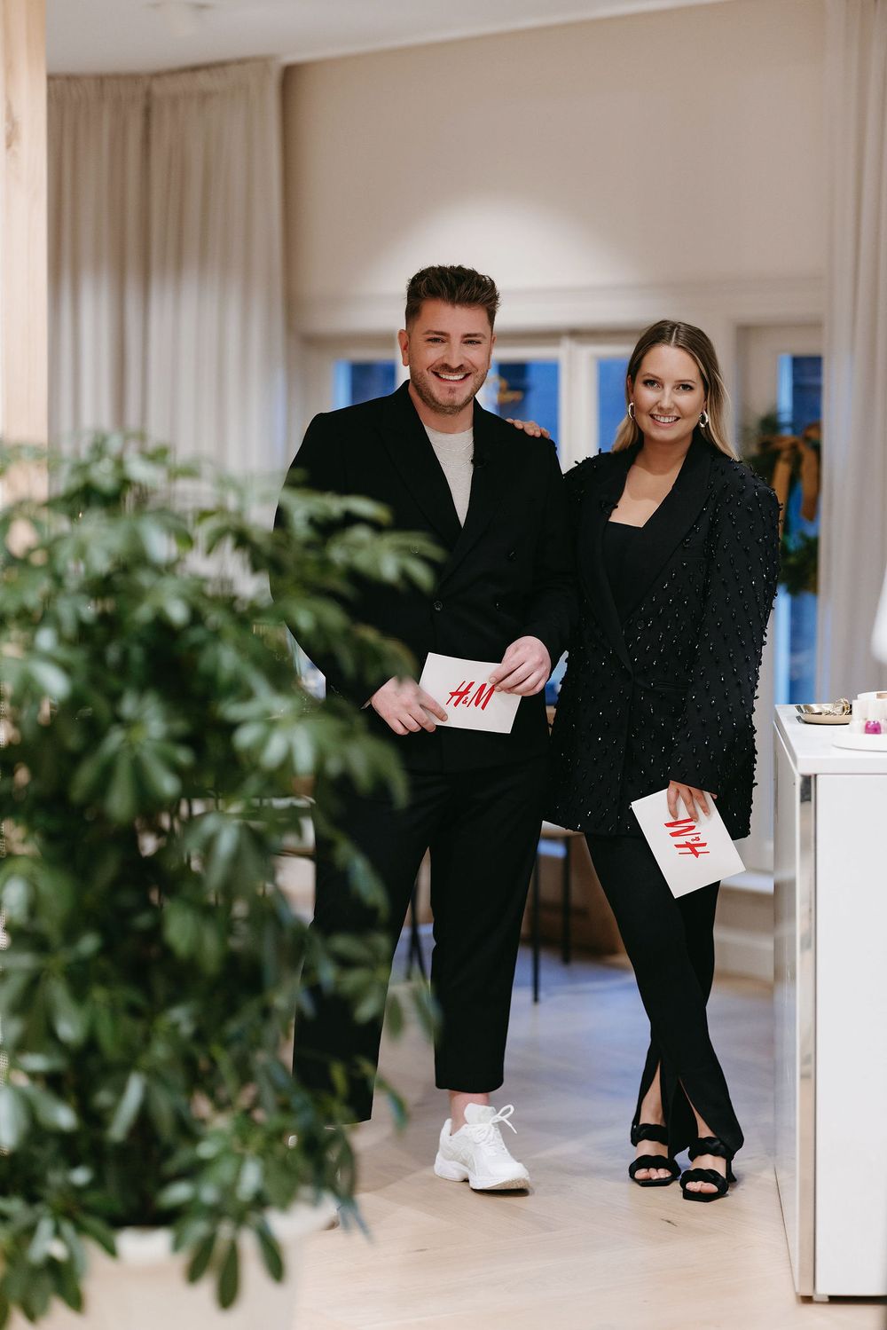 Styled pair holding H&M bags in a modern retail setting with indoor plants.
