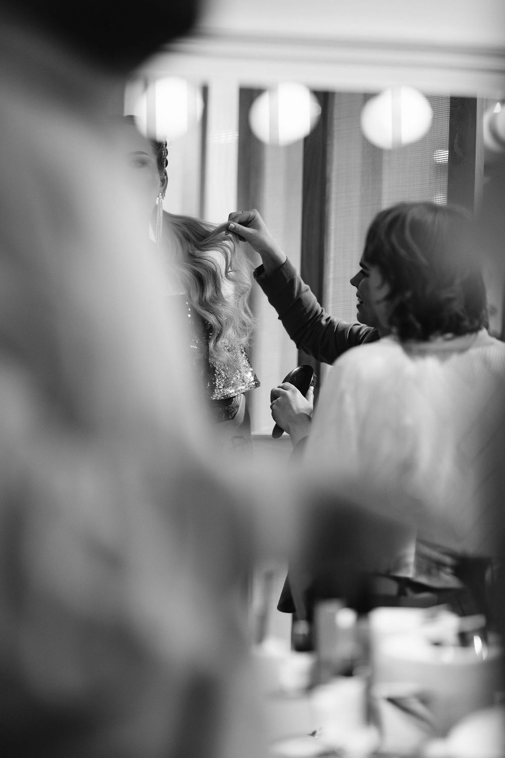 Black and white image of bridal preparation in a dressing room with mirrors and lighting.