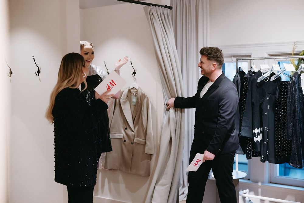 People discussing clothing items in upscale retail space with hanging garments.