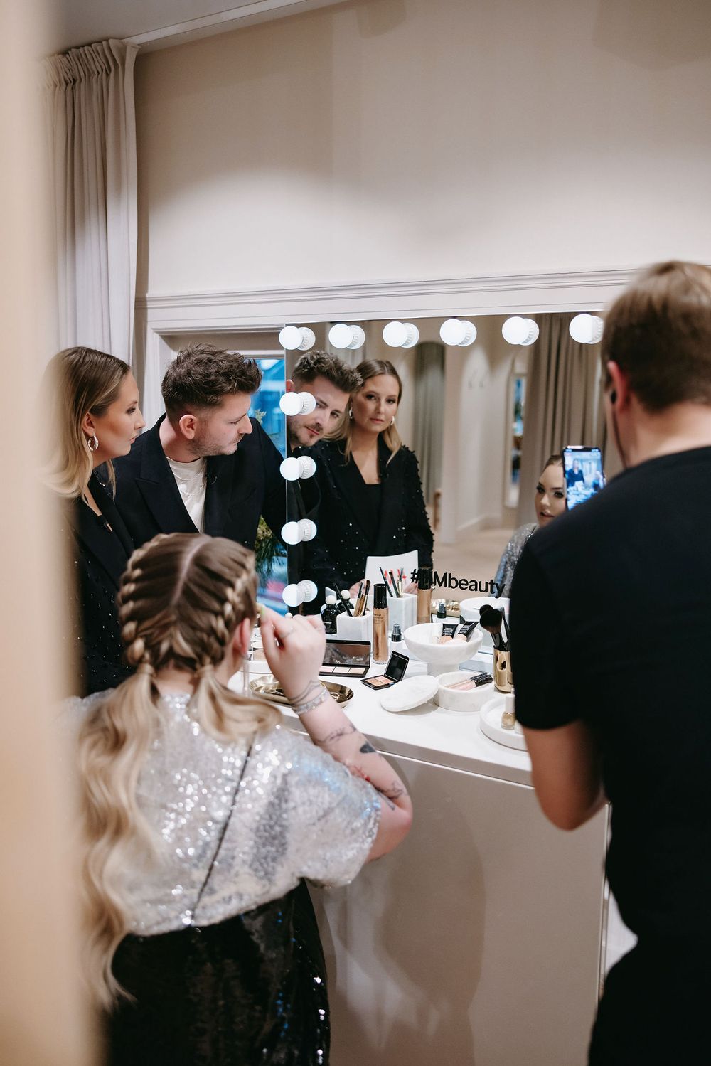 Behind the scenes preparation at a beauty counter with stylists working at a vanity mirror station.