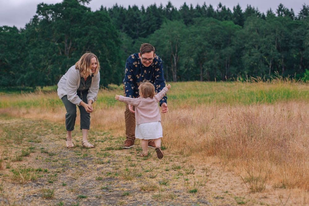 A family plays together on a dirt path surrounded by tall grass and evergreen trees. Spokane Liberty Lake Photographer Family Photographer