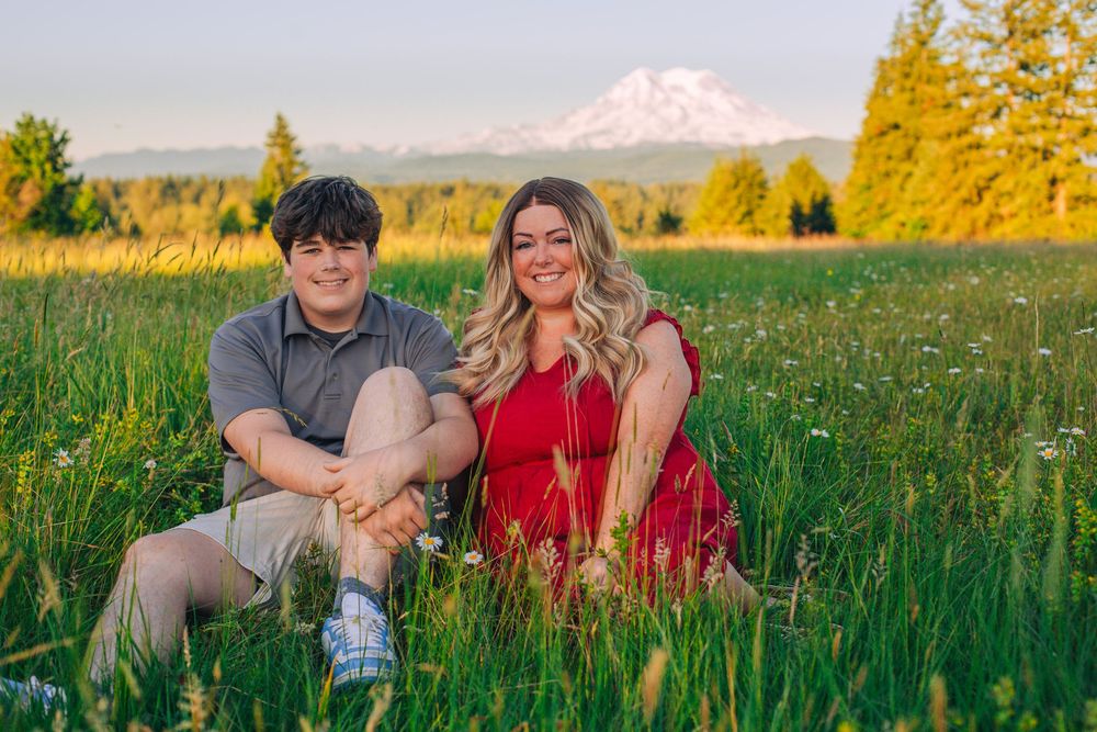A couple sits in a lush green field with Mount Hood visible in the distance. Spokane Liberty Lake Photographer Family Photographer