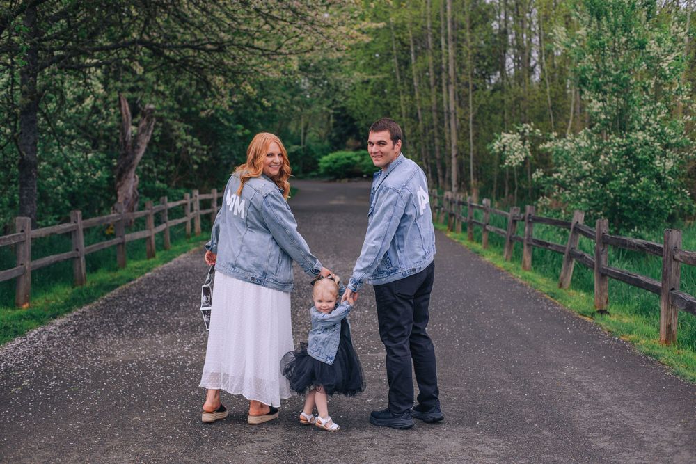 A family holds hands while standing on a tree-lined gravel path. Spokane Liberty Lake Photographer Family Photographer