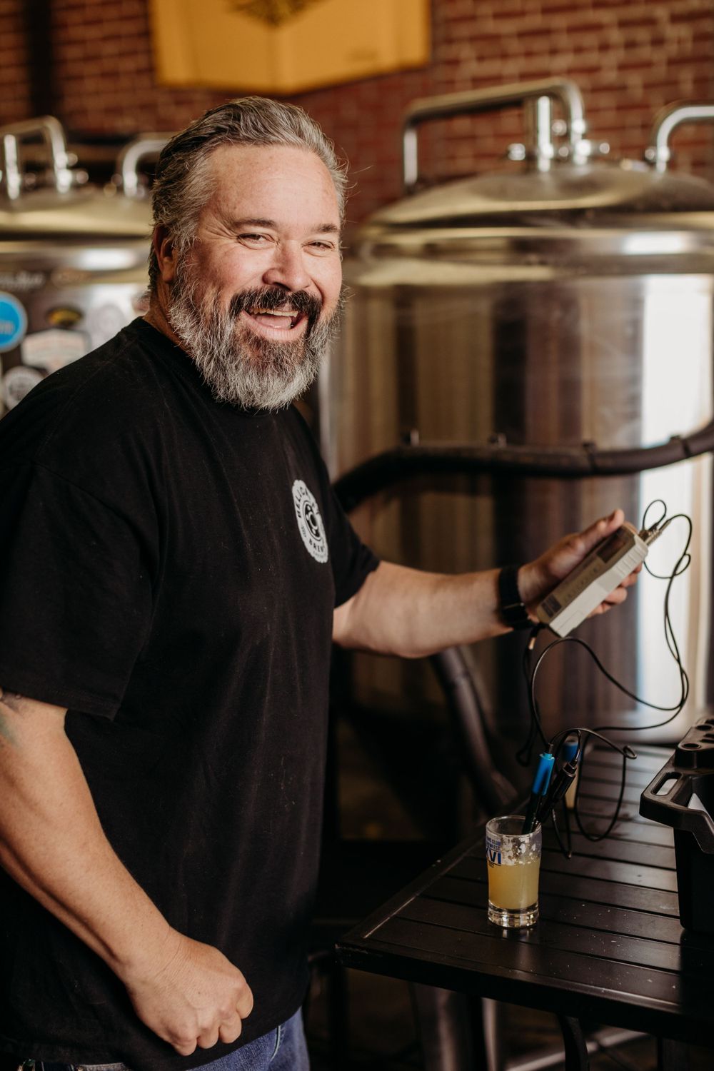 Brewery worker in black shirt inspecting equipment in industrial brewing facility.
