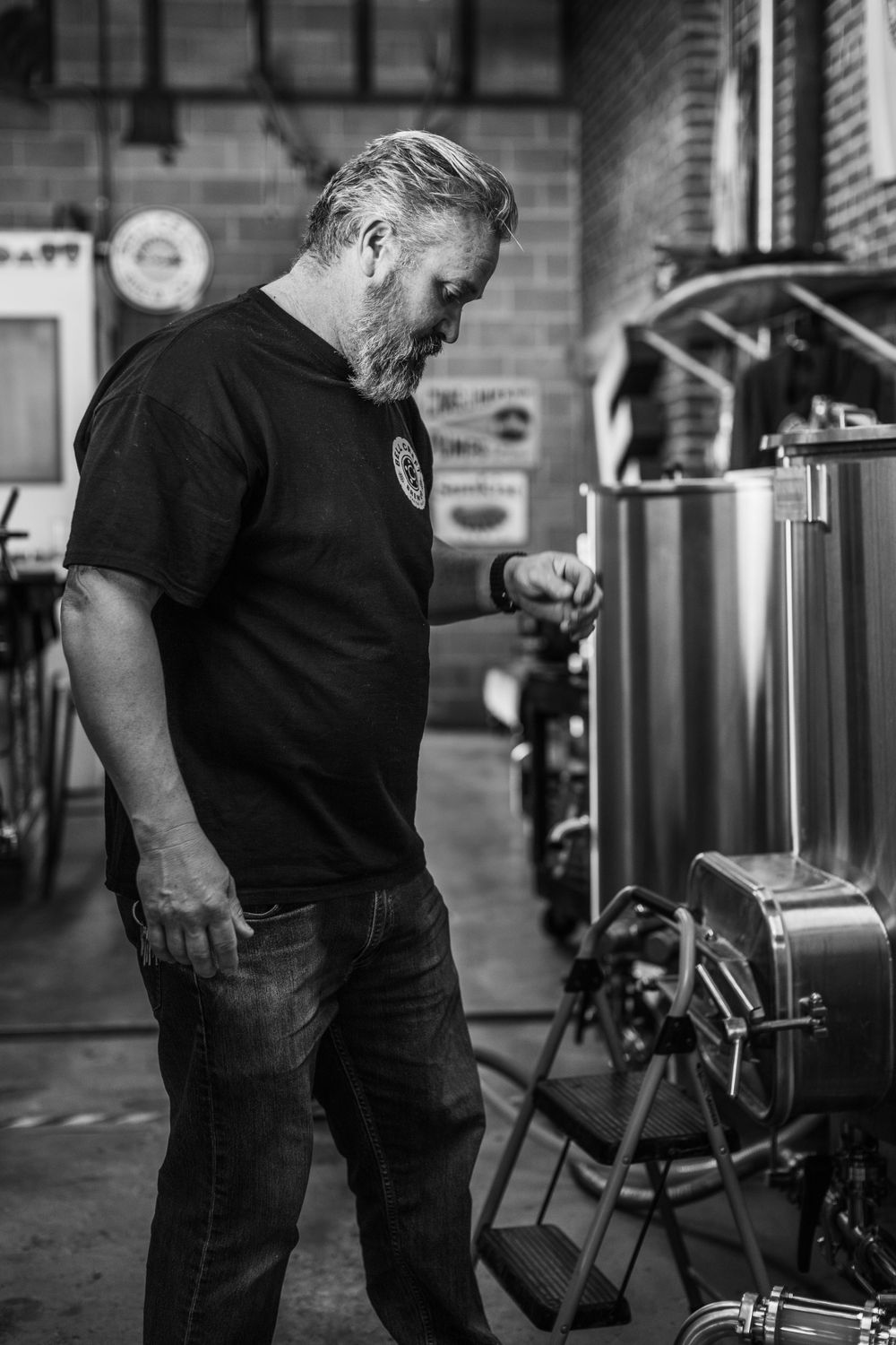 Craft brewery worker monitoring stainless steel brewing equipment in industrial setting.