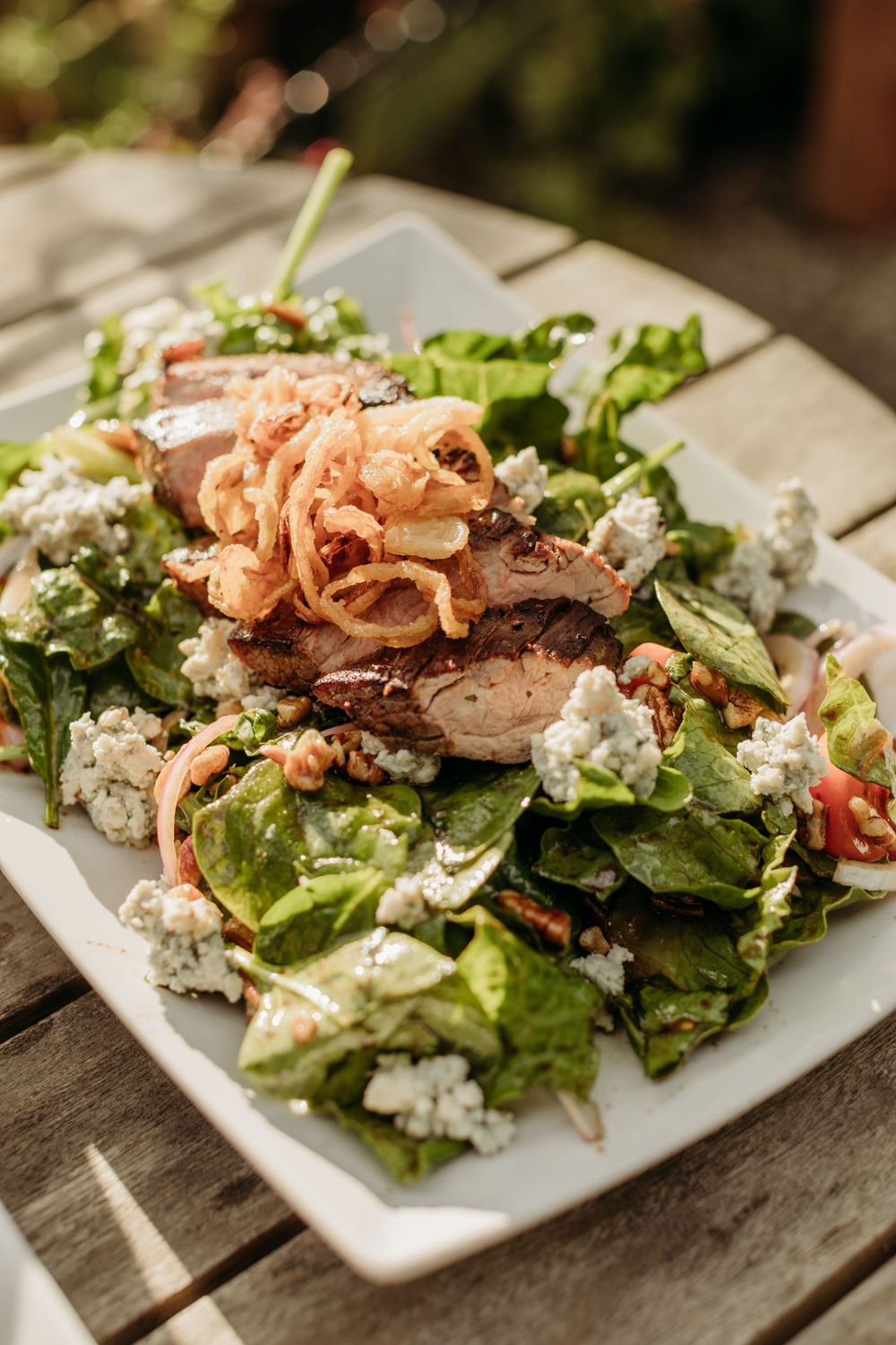 Fresh salad with mixed greens, crumbled blue cheese, crispy onions and grilled meat on a white plate.